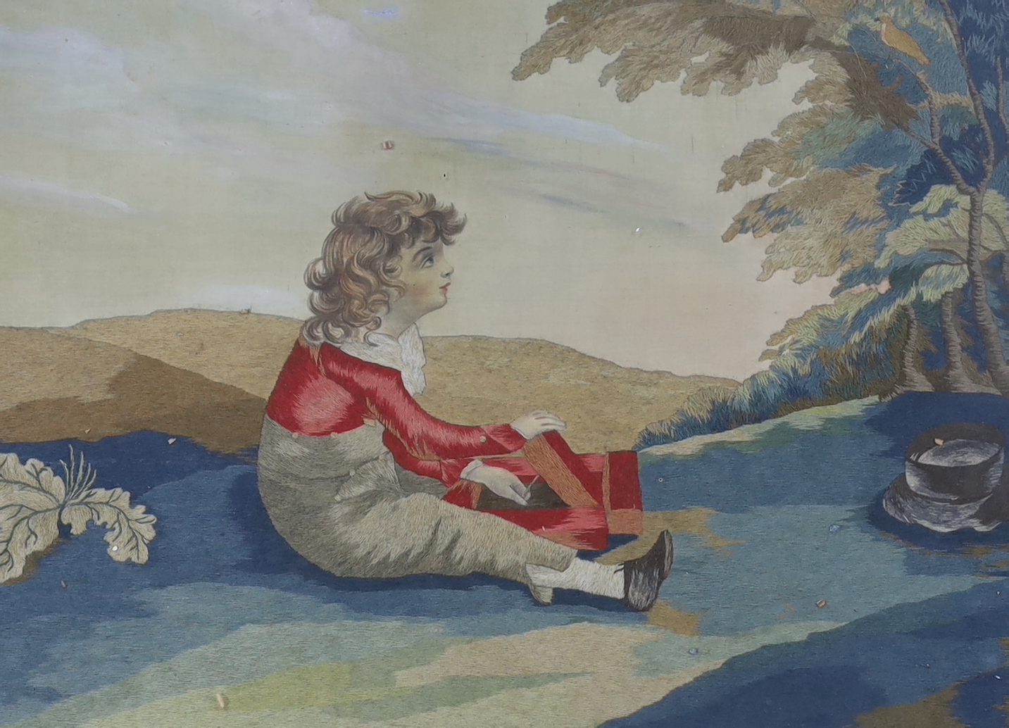 A Regency silk and woolwork picture of a boy sitting under a tree with a bird catcher, 55cm wide x 40cm high